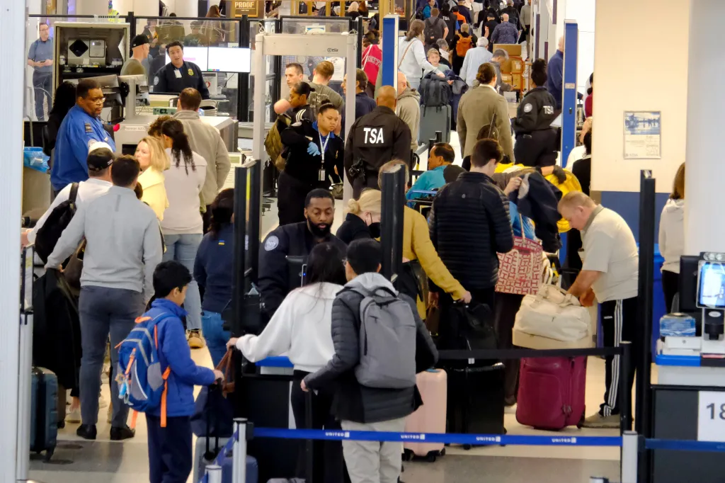Travelers and TSA security personnel in a busy airport security line.
