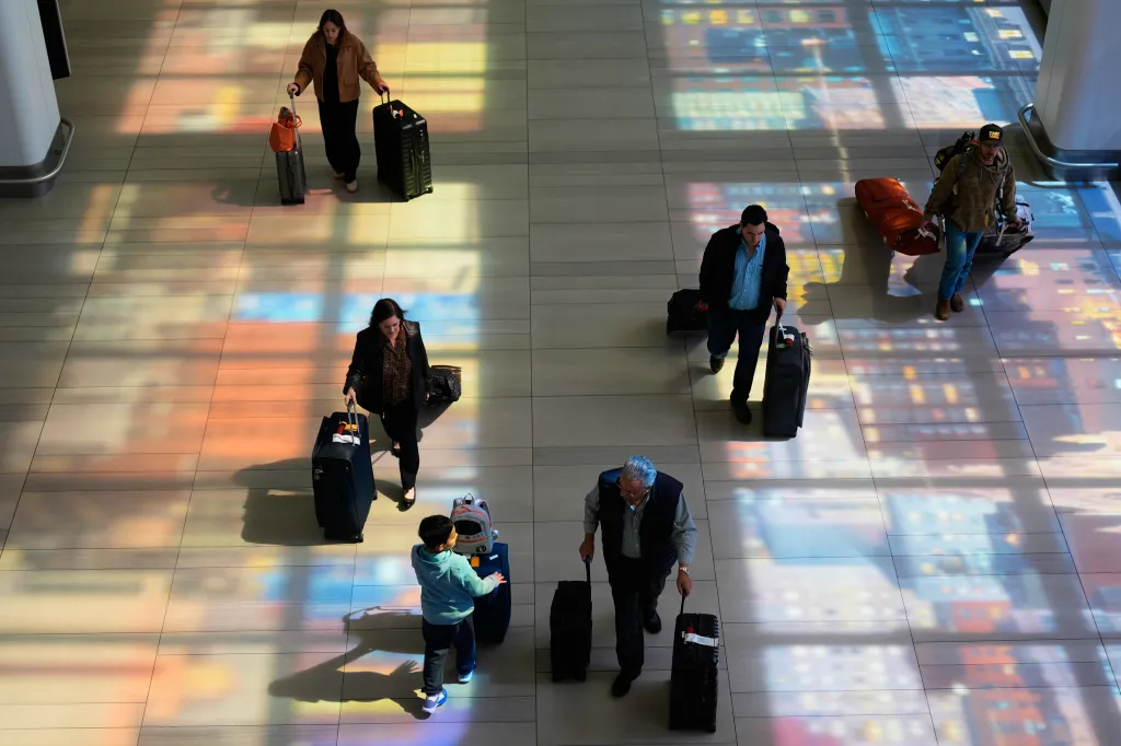 Travelers with luggage walk through LaGuardia Airport, with colorful shadows from stained-glass windows cast on the floor.