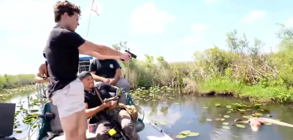 Streamer Braden Eric Peters aims a handgun over the water from an airboat in the Florida Everglades.