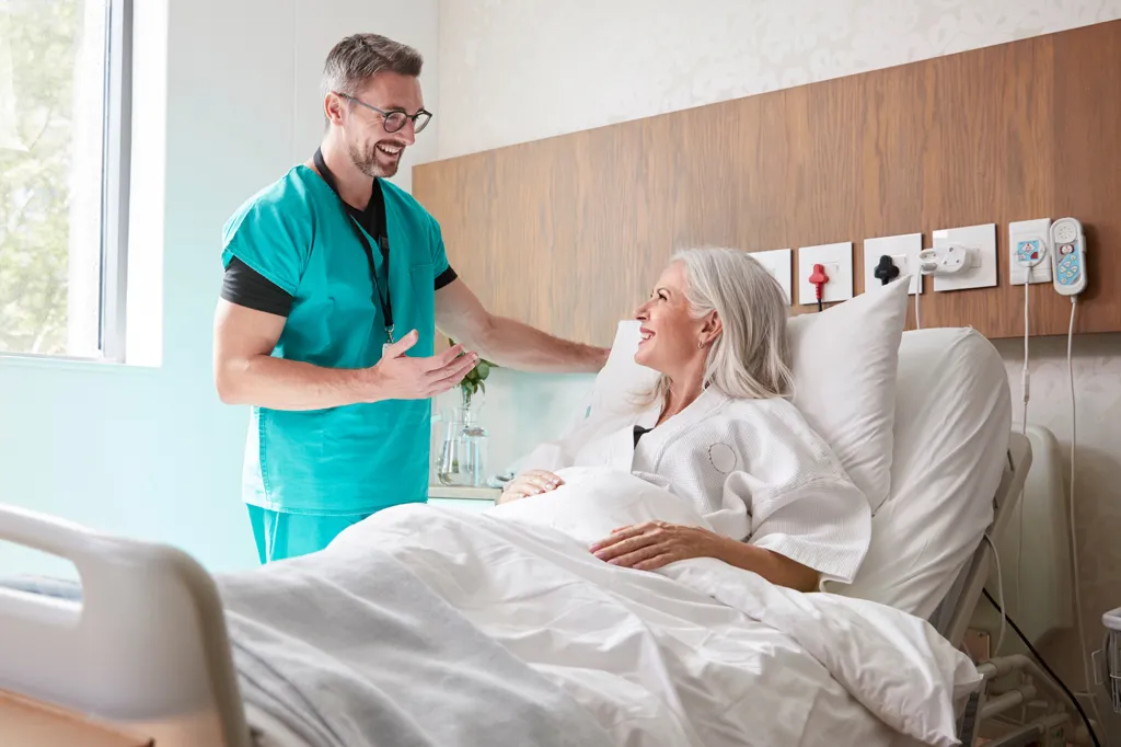 Male surgeon talking with a mature female patient in a hospital bed.