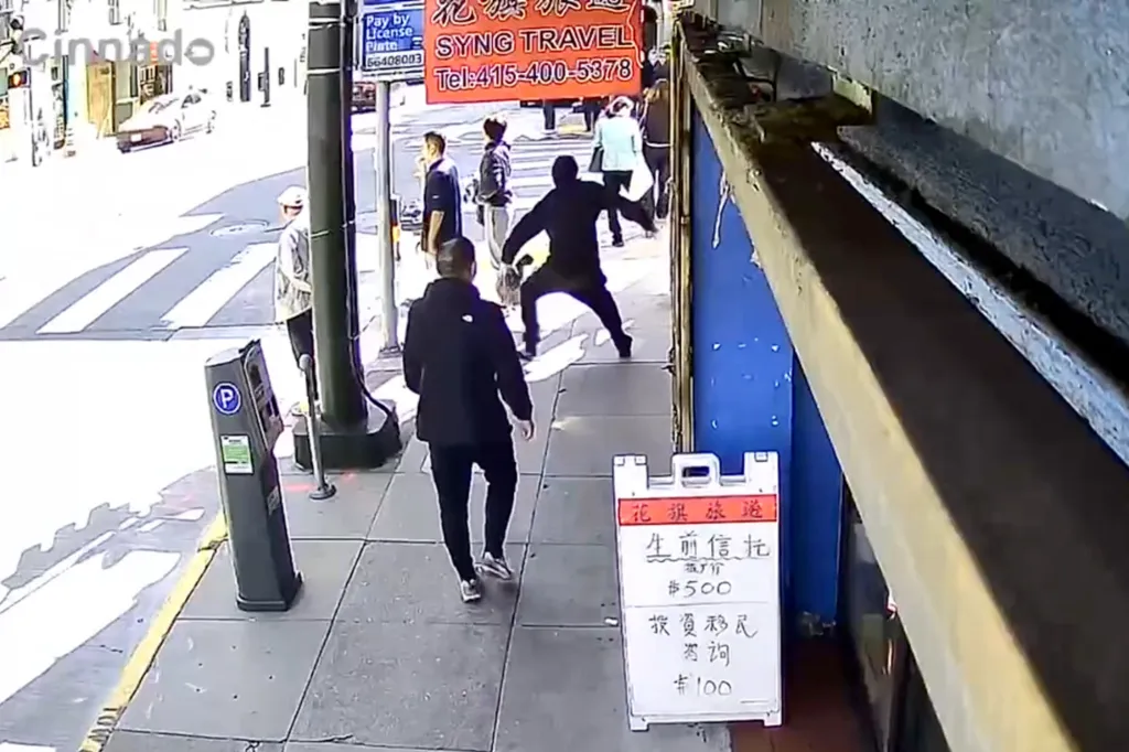 Surveillance footage shows a man in a black hoodie stabbing another man on a sidewalk.