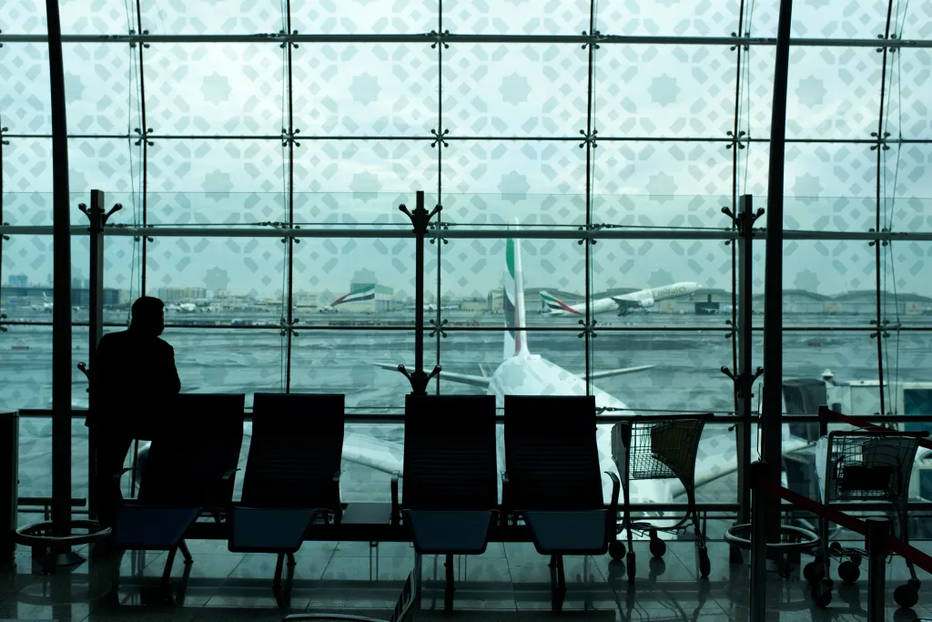A silhouette of a man looking out an airport window at a plane taking off.