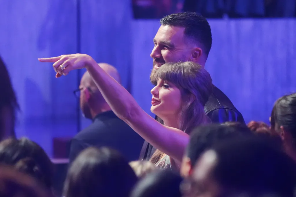 Taylor Swift pointing in the audience with Travis Kelce behind her.
