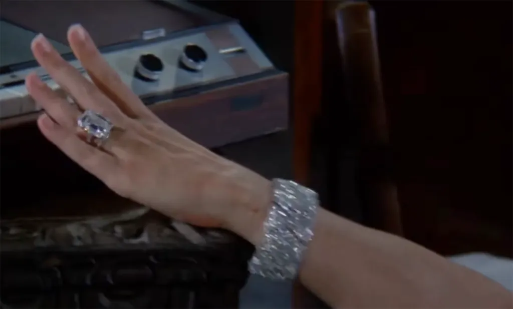 A close-up of a person's hand wearing a large emerald-cut diamond ring and a wide, sparkling diamond bracelet.