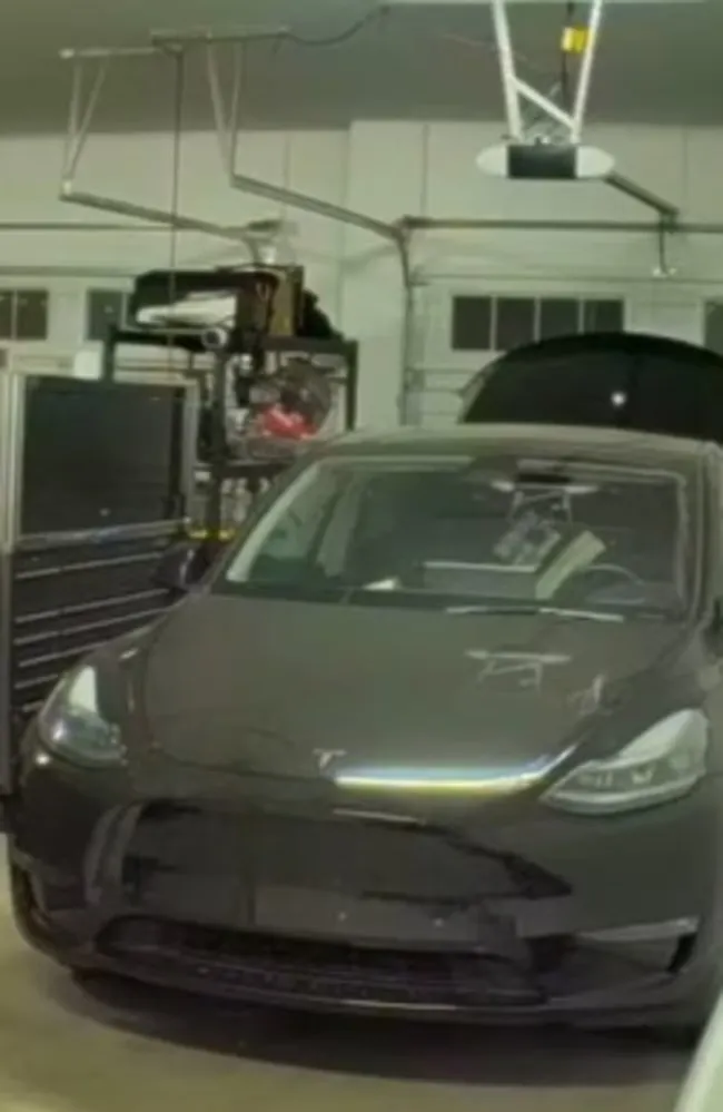 A dark grey Tesla with an open hood is parked in a garage.