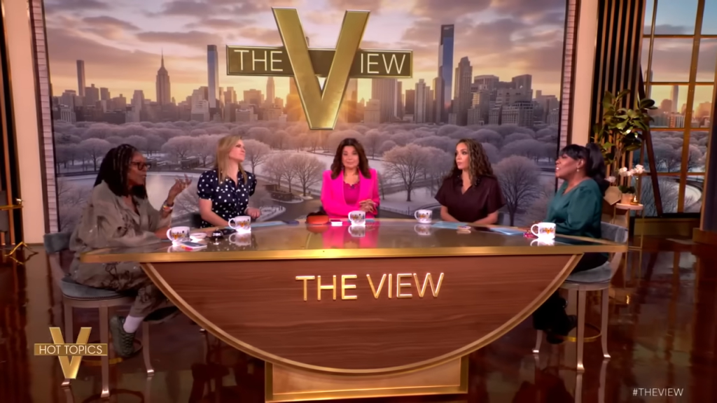 The five co-hosts of The View, Whoopi Goldberg, Sara Haines, Ana Navarro, Sunny Hostin, and Sherri Shepherd, sitting at their debate table.