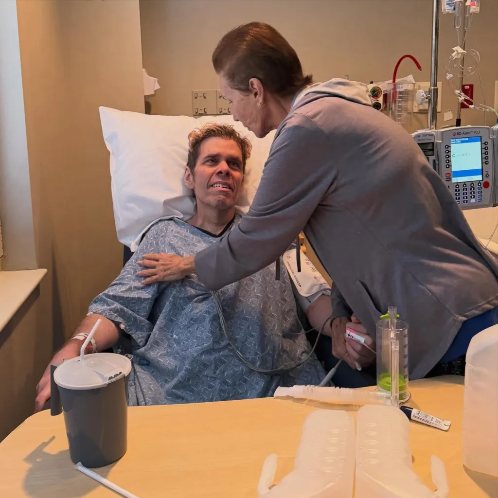 Perez Hilton in a hospital bed is comforted by a woman.
