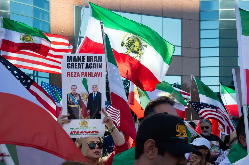 Protesters waving American and Iranian flags, with a sign showing images of Reza Pahlavi and his father, Mohammad Reza Pahlavi, at a rally.
