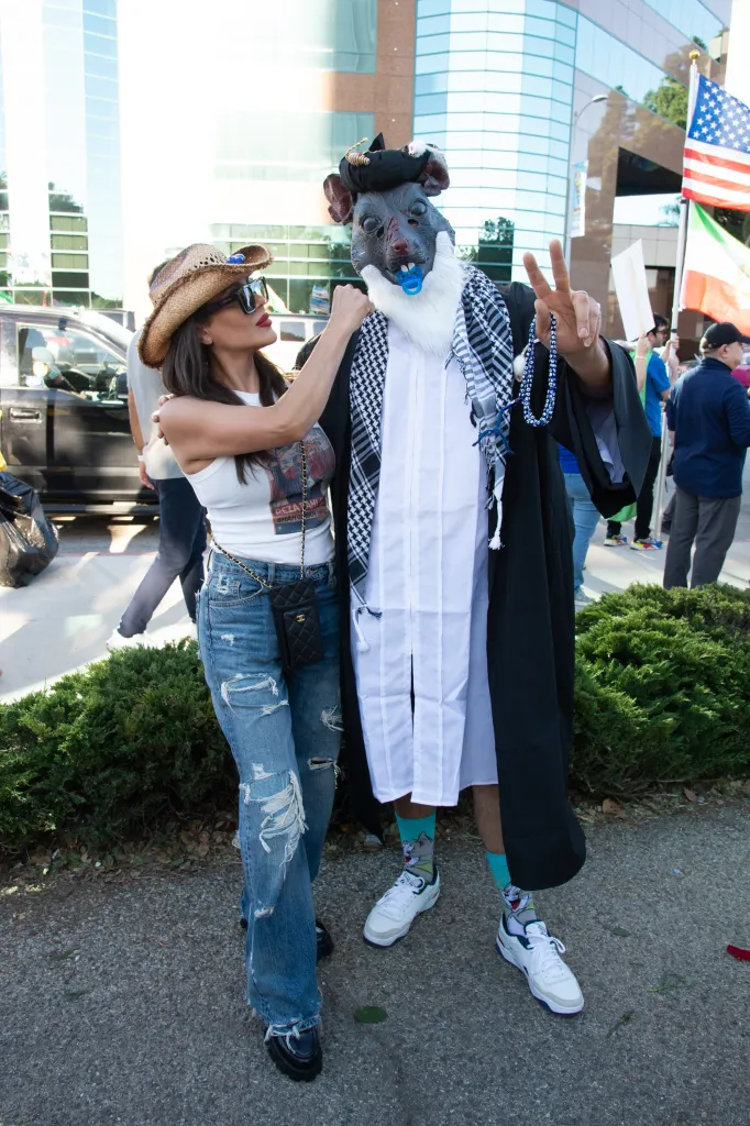 A person in a rat mask with a pacifier and a woman in a cowboy hat at a protest in Westwood, CA.