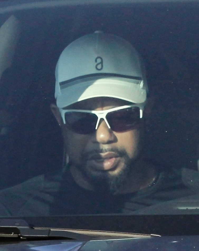 Tiger Woods in a white cap and sunglasses, seen through a car window.