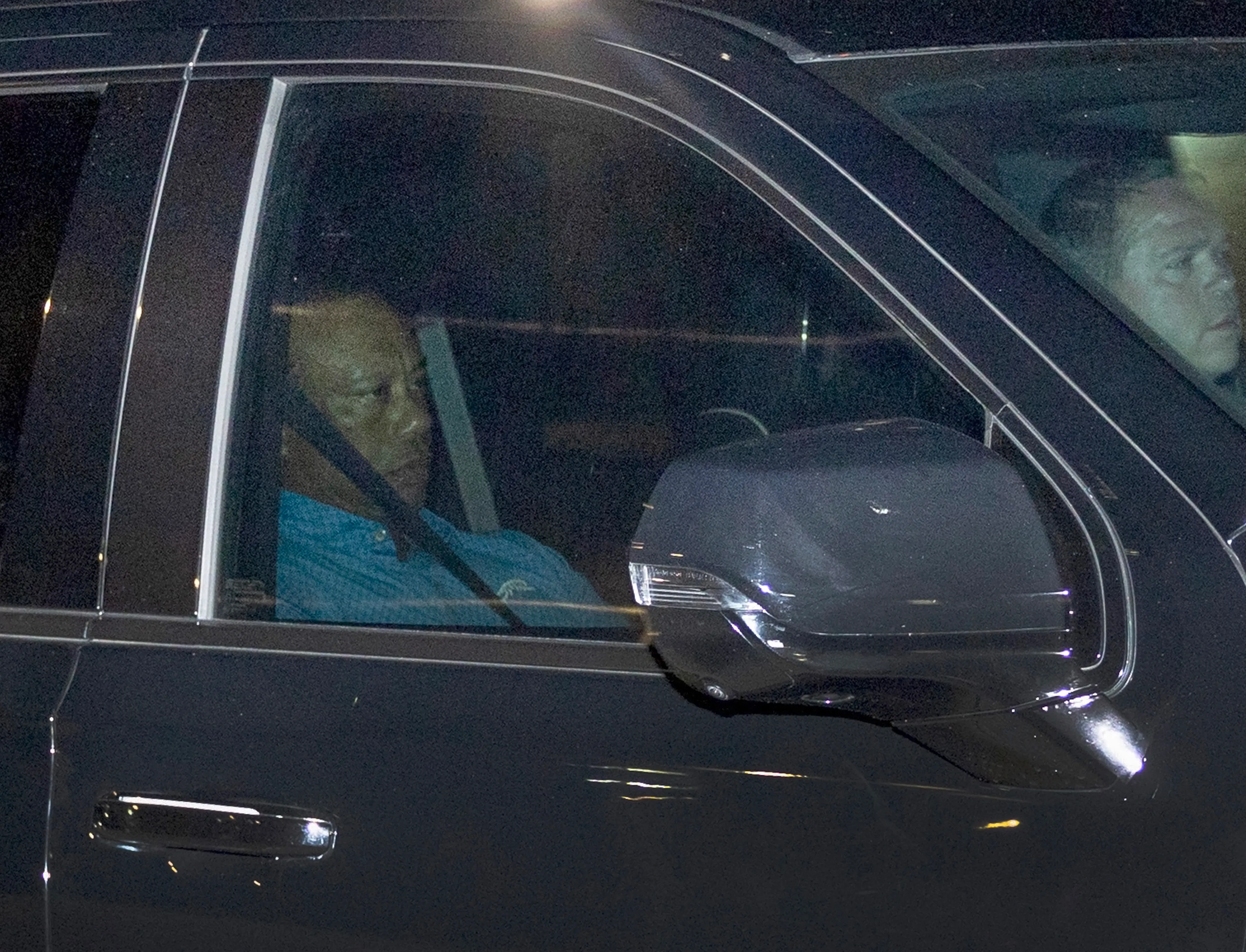 Tiger Woods in a blue shirt driving a dark vehicle.