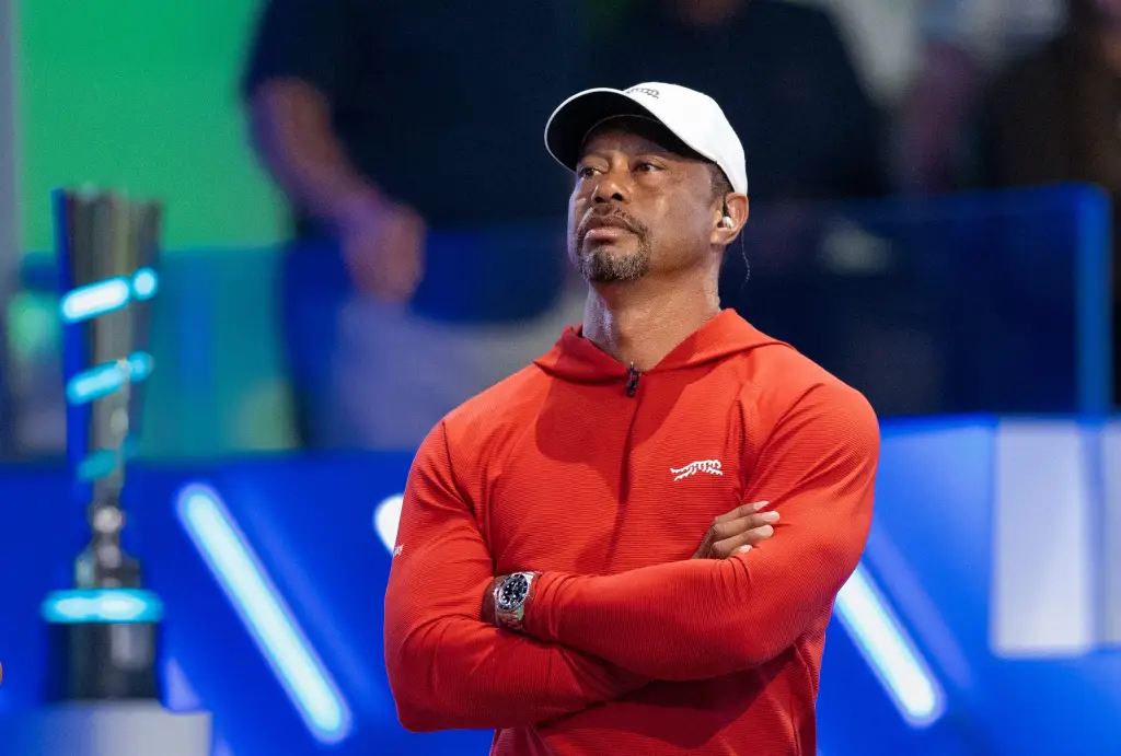 Tiger Woods in a red hoodie and white cap, watching a TGL match.