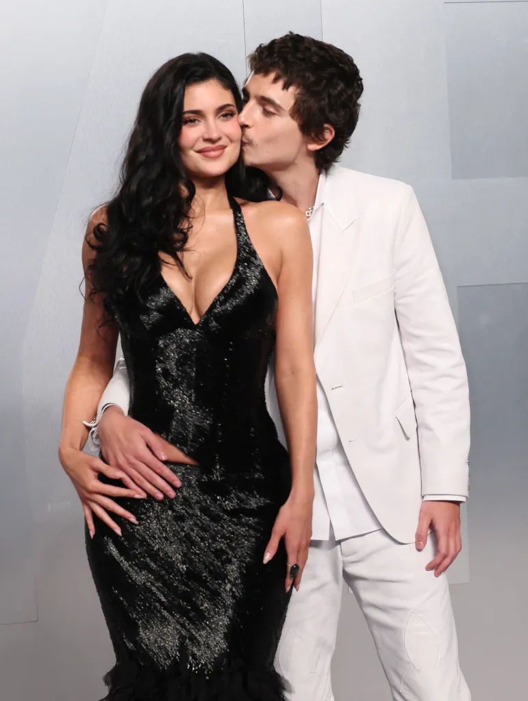 Timothée Chalamet, in a white suit, kissing Kylie Jenner, in a black sparkling gown, on the cheek at the Vanity Fair Oscars party.