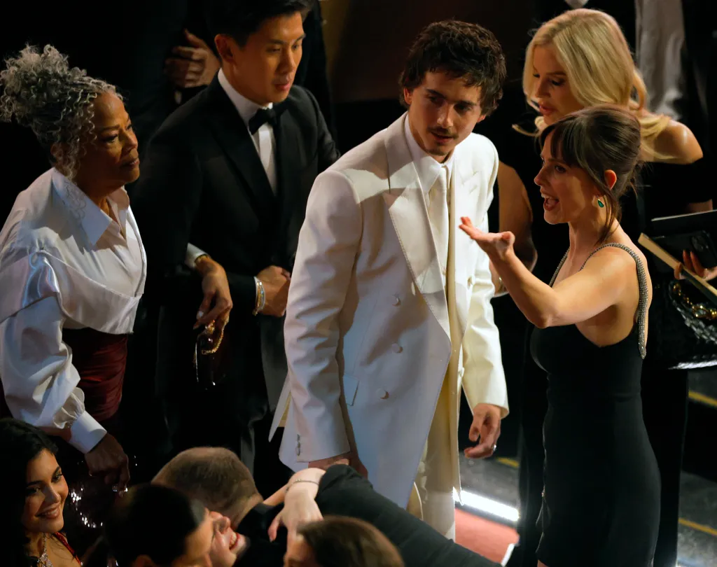 Timothee Chalamet, in a white suit, with Pauline Chalamet, in a black mini dress, talking to Donna Jordan, in a white shirt and burgundy skirt.