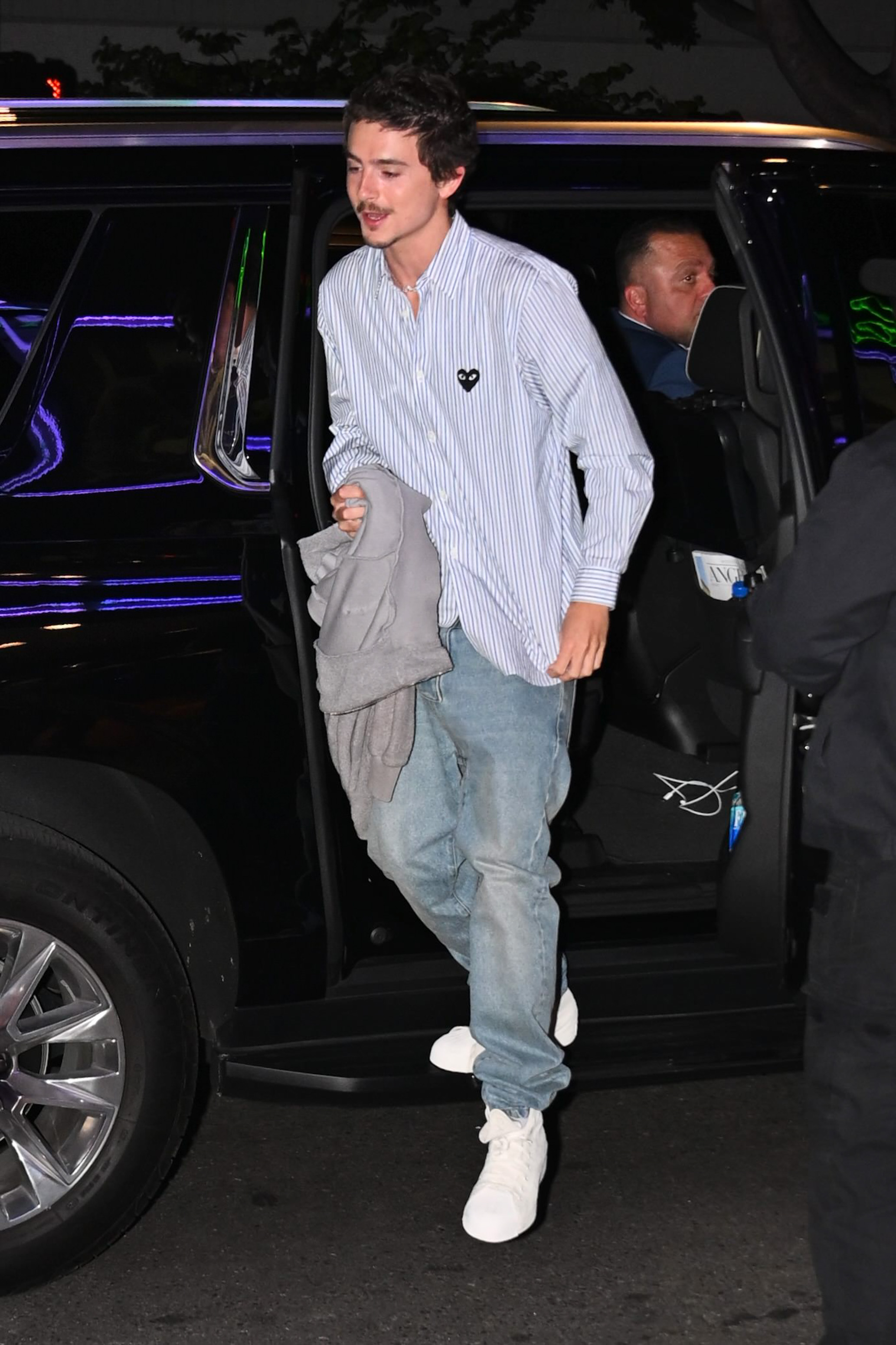 Timothée Chalamet exits a dark SUV, holding a gray sweatshirt.