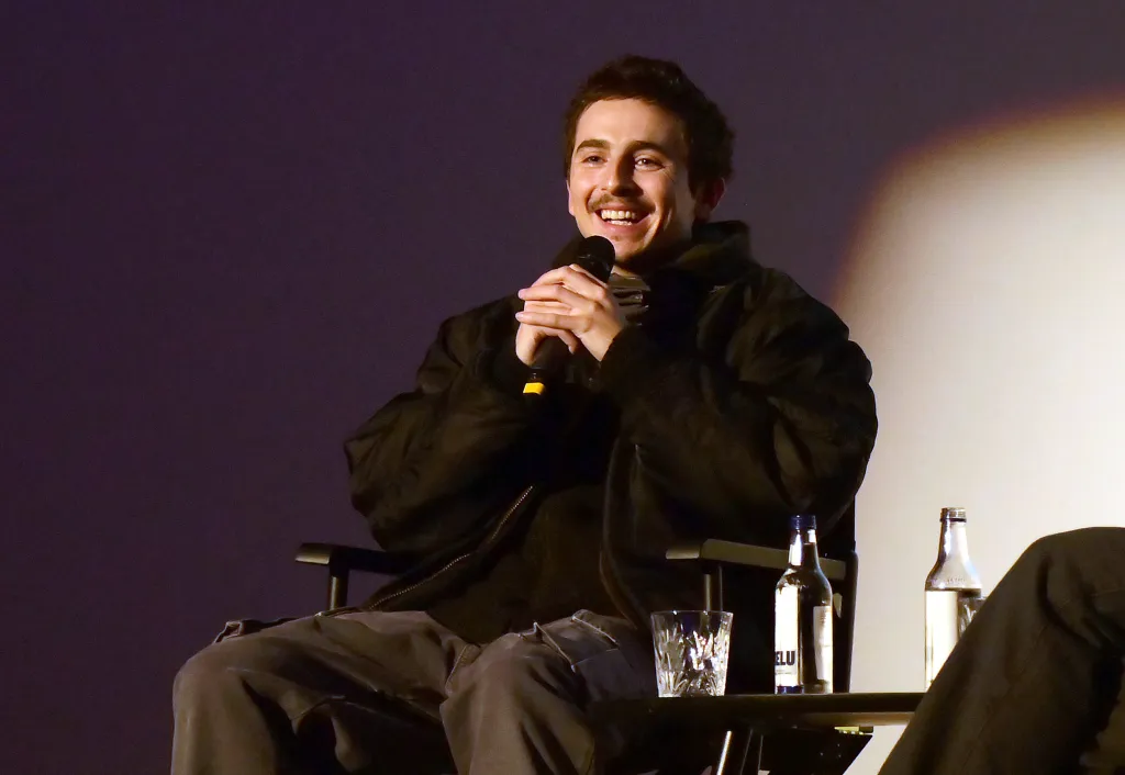 Timothée Chalamet smiling and holding a microphone while speaking on stage during a Q&A session.