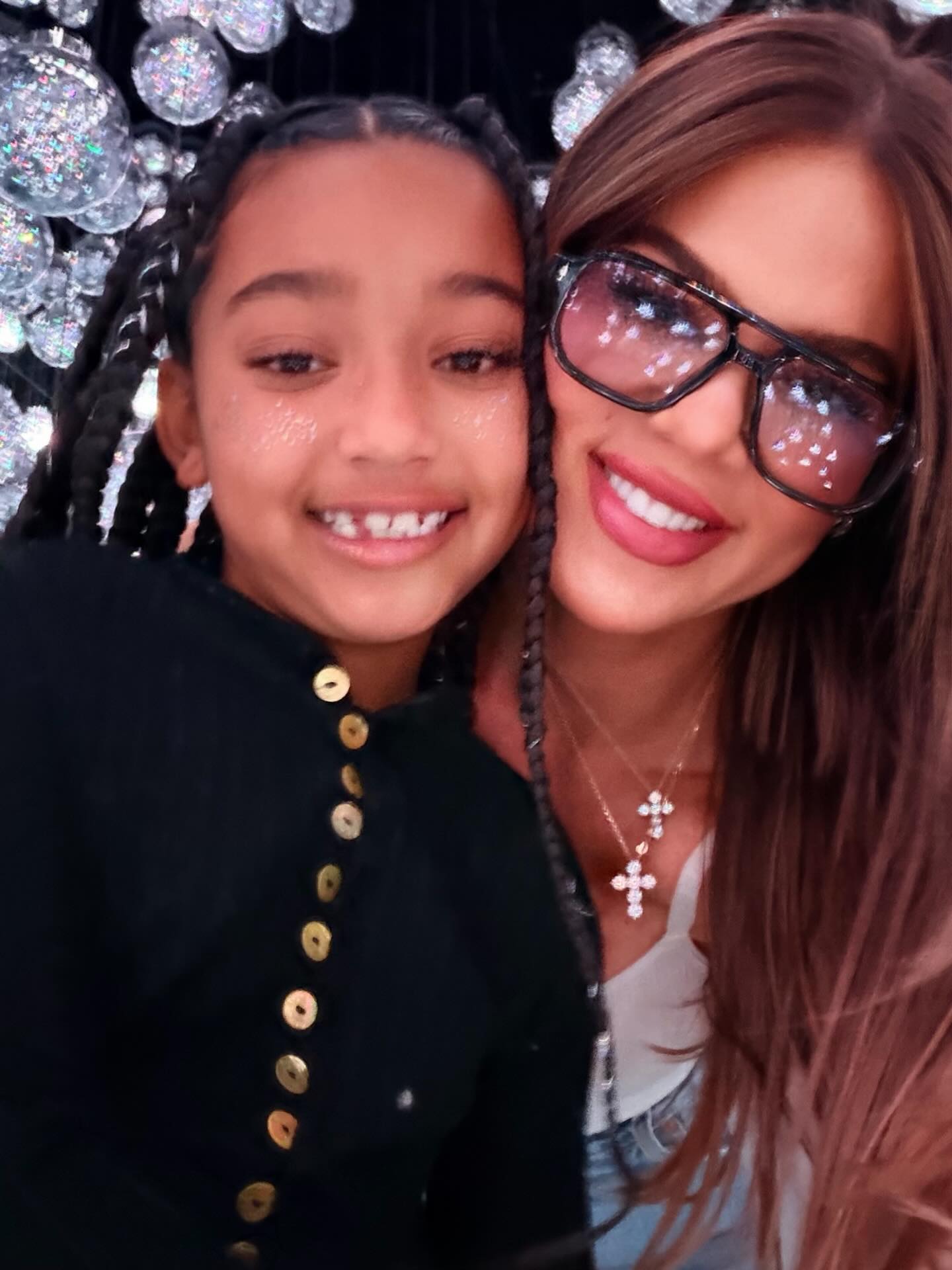 Khloé Kardashian smiling in large sunglasses next to True Thompson.