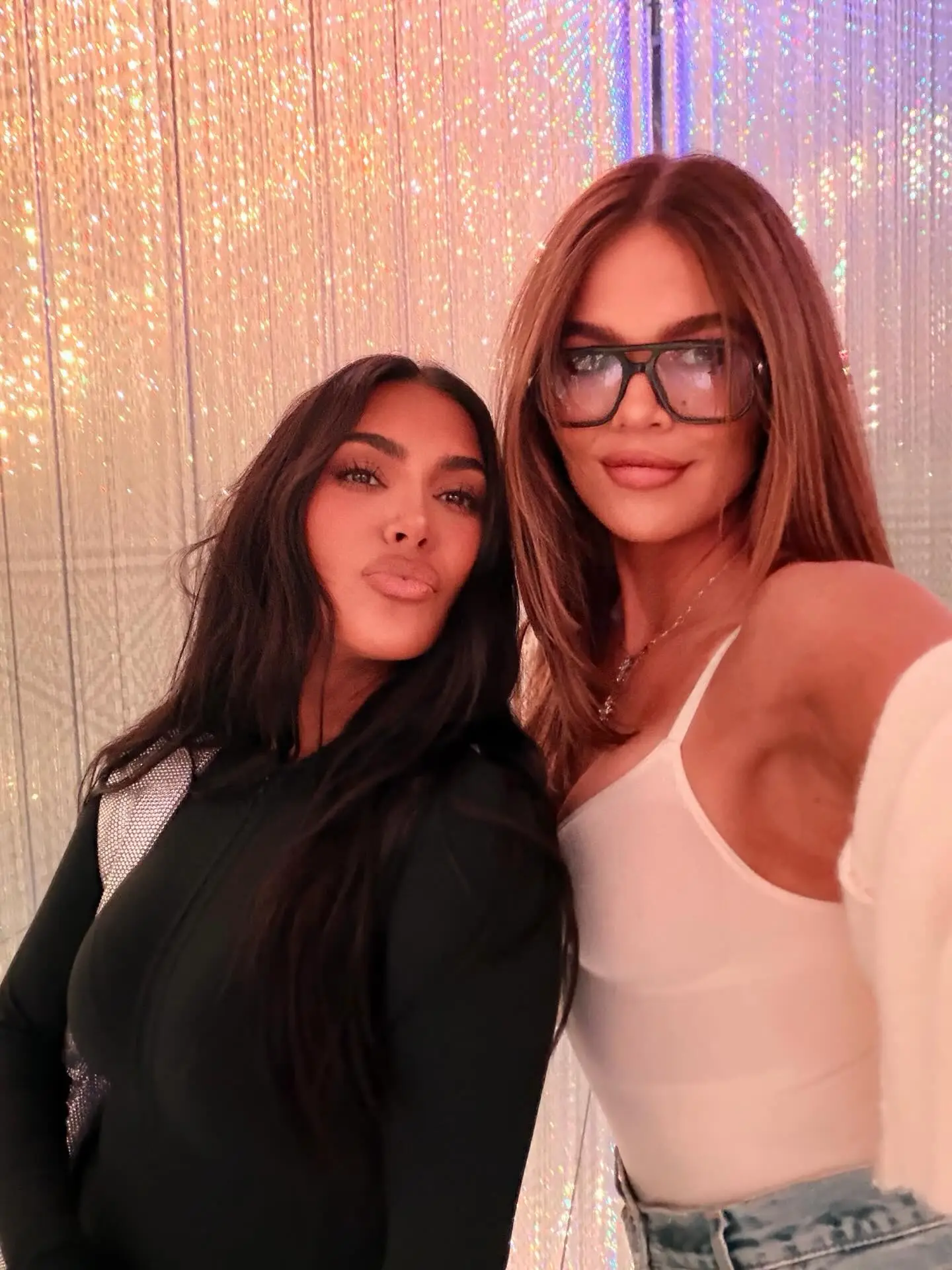 Kim Kardashian (left) and Khloé Kardashian pose for a selfie with a sparkly background.