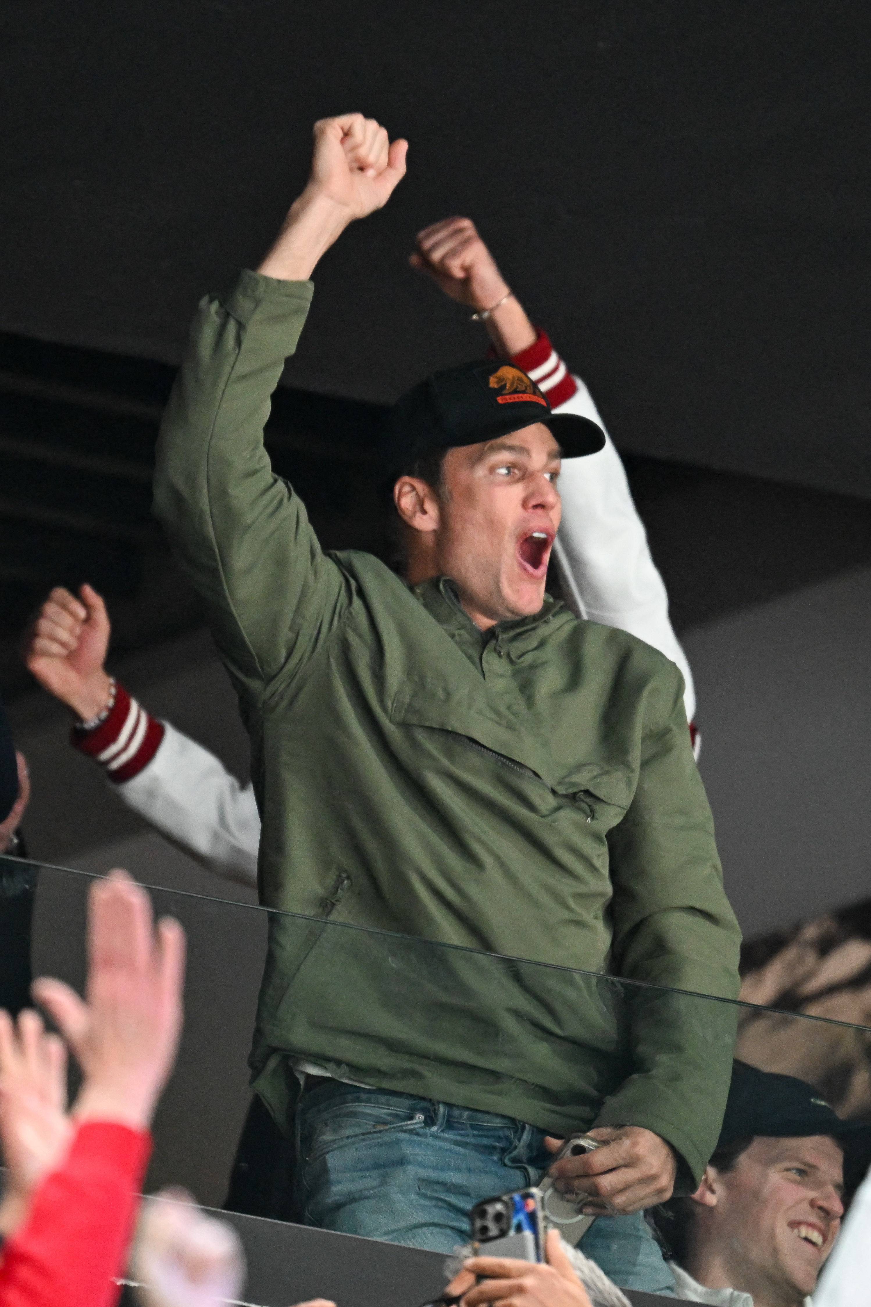 Tom Brady cheers, fist raised, at an ice hockey game.