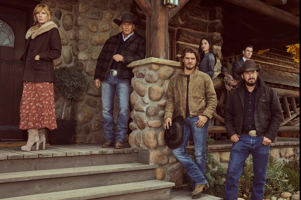 The cast of Yellowstone stands on the porch and steps of a rustic lodge.