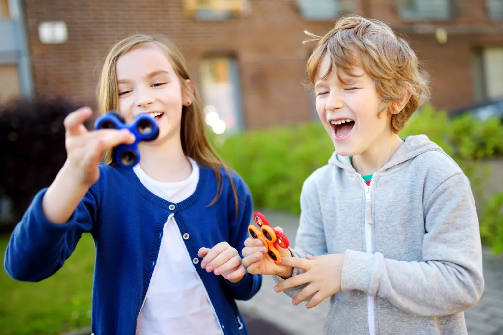 Two children laugh while playing with fidget spinners.