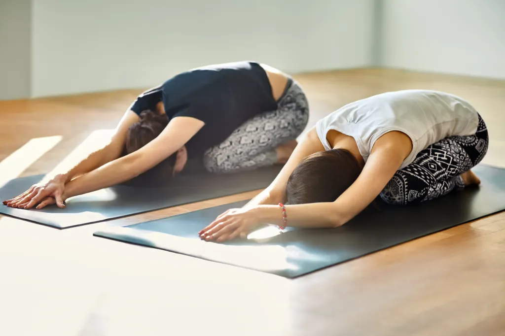 Two young women doing Child's Pose (Balasana) on yoga mats.