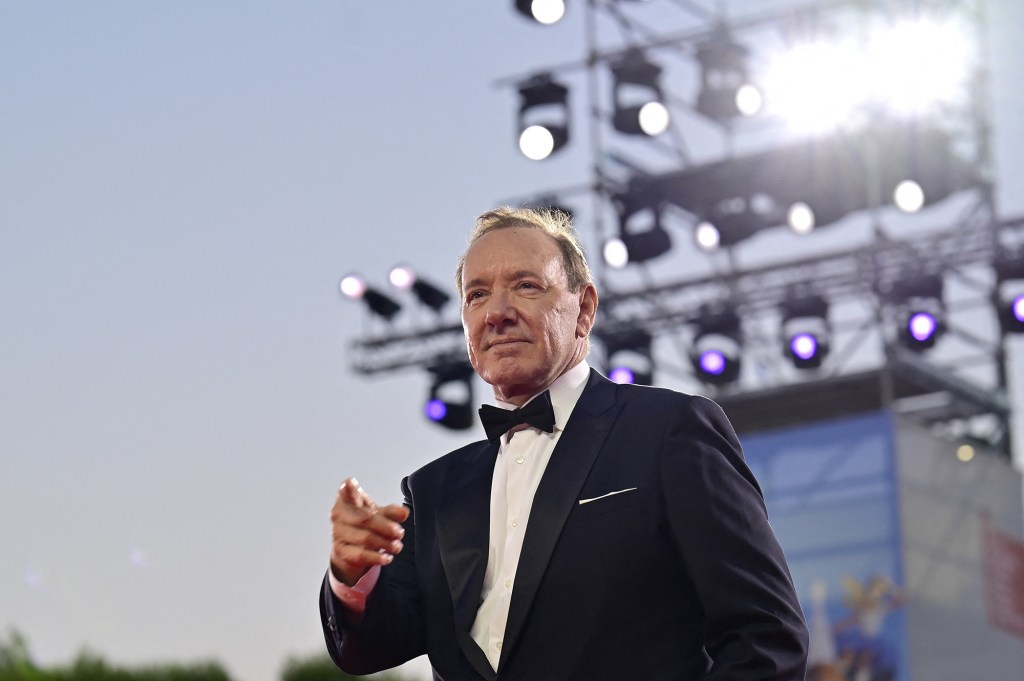 Actor Kevin Spacey on the red carpet at the Venice Film Festival, pointing his finger forward.