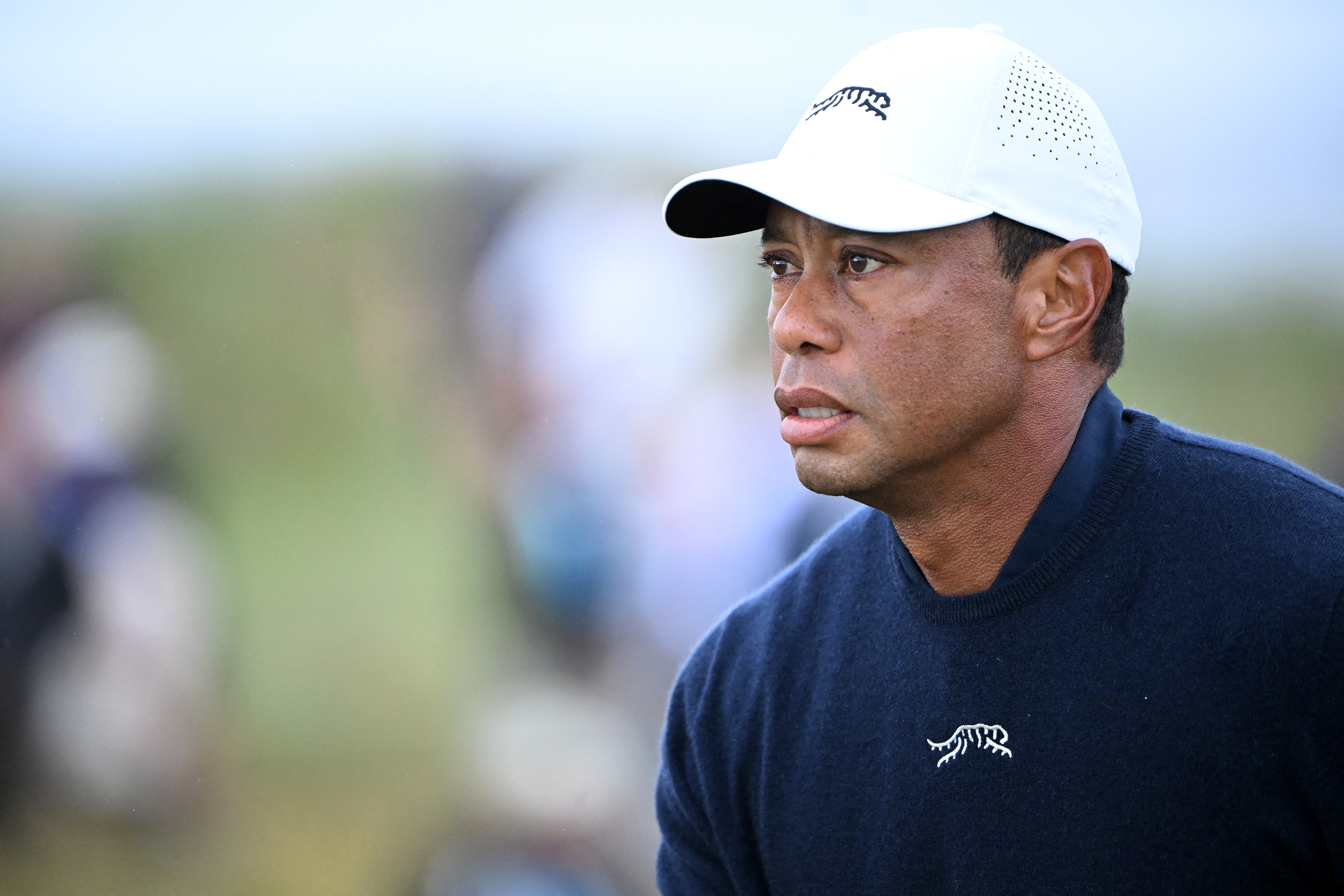 Golfer Tiger Woods wearing a white cap and navy sweater.