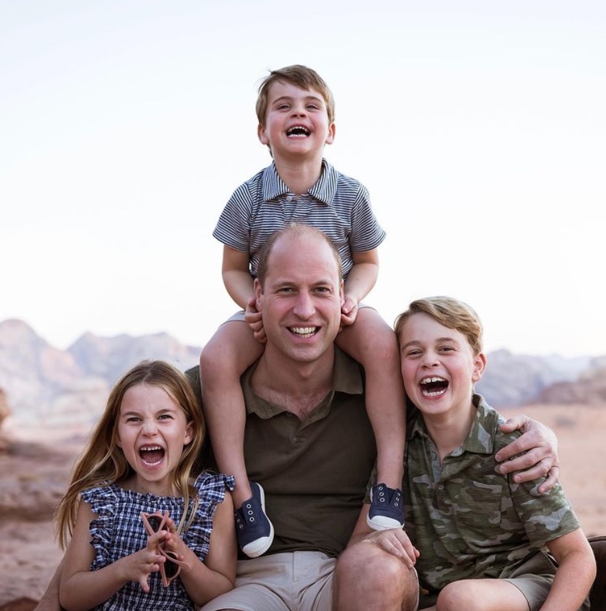 Prince William sitting with his three children, Prince George, Princess Charlotte, and Prince Louis, in a desert landscape.