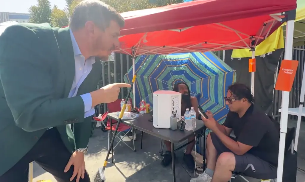 Man in a green jacket confronting other men under a red tent.