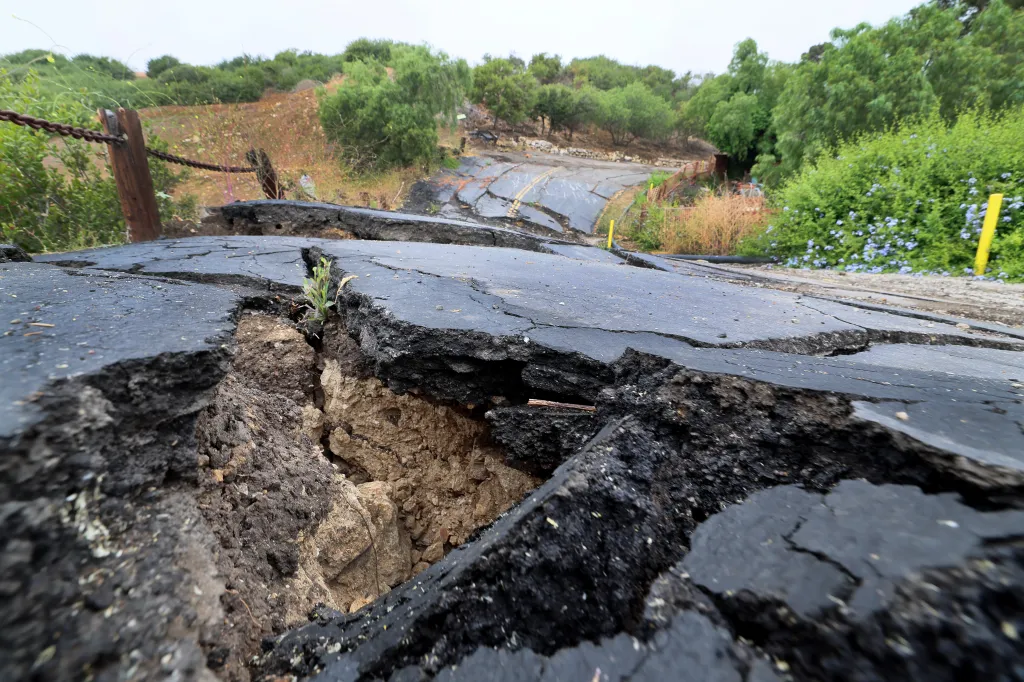 A severely damaged asphalt road with large cracks and raised sections due to a landslide in Rancho Palos Verdes, California.