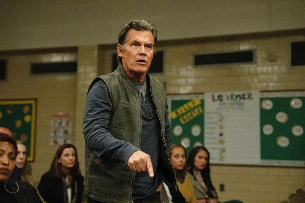 Josh Brolin in a gray vest pointing down as he speaks to an audience.