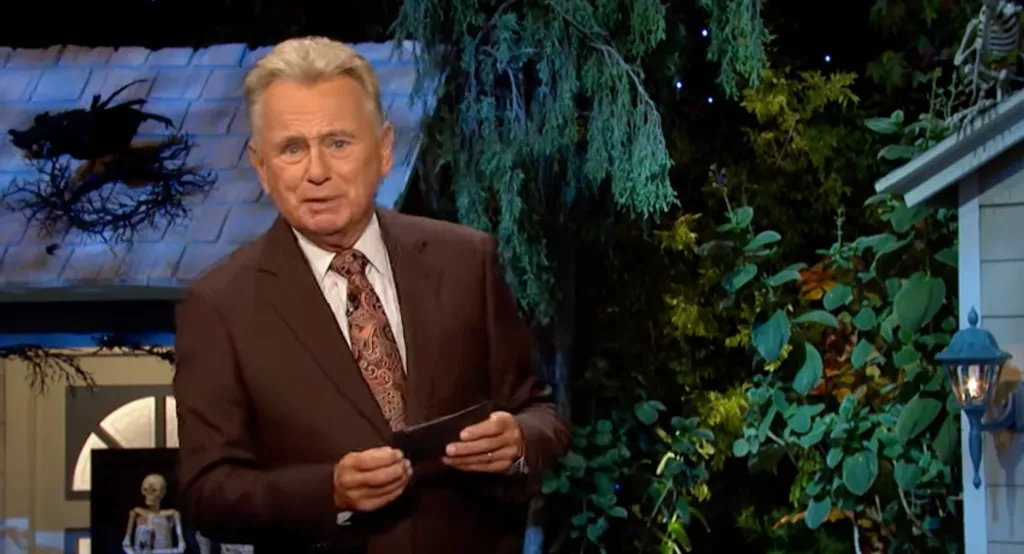Pat Sajak holding a card on a Halloween-themed set.