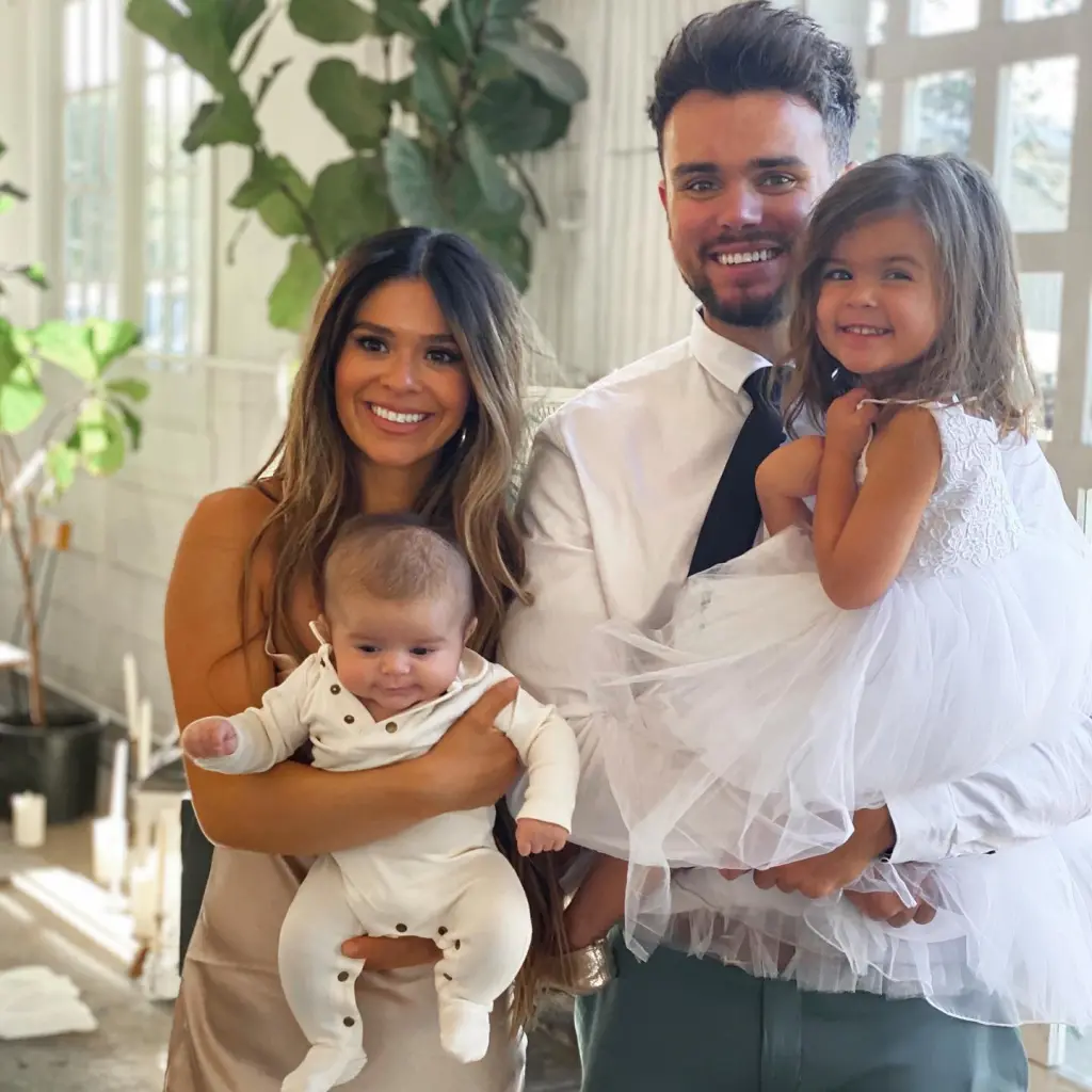 A family of four, with two parents and two young children, posing and smiling.