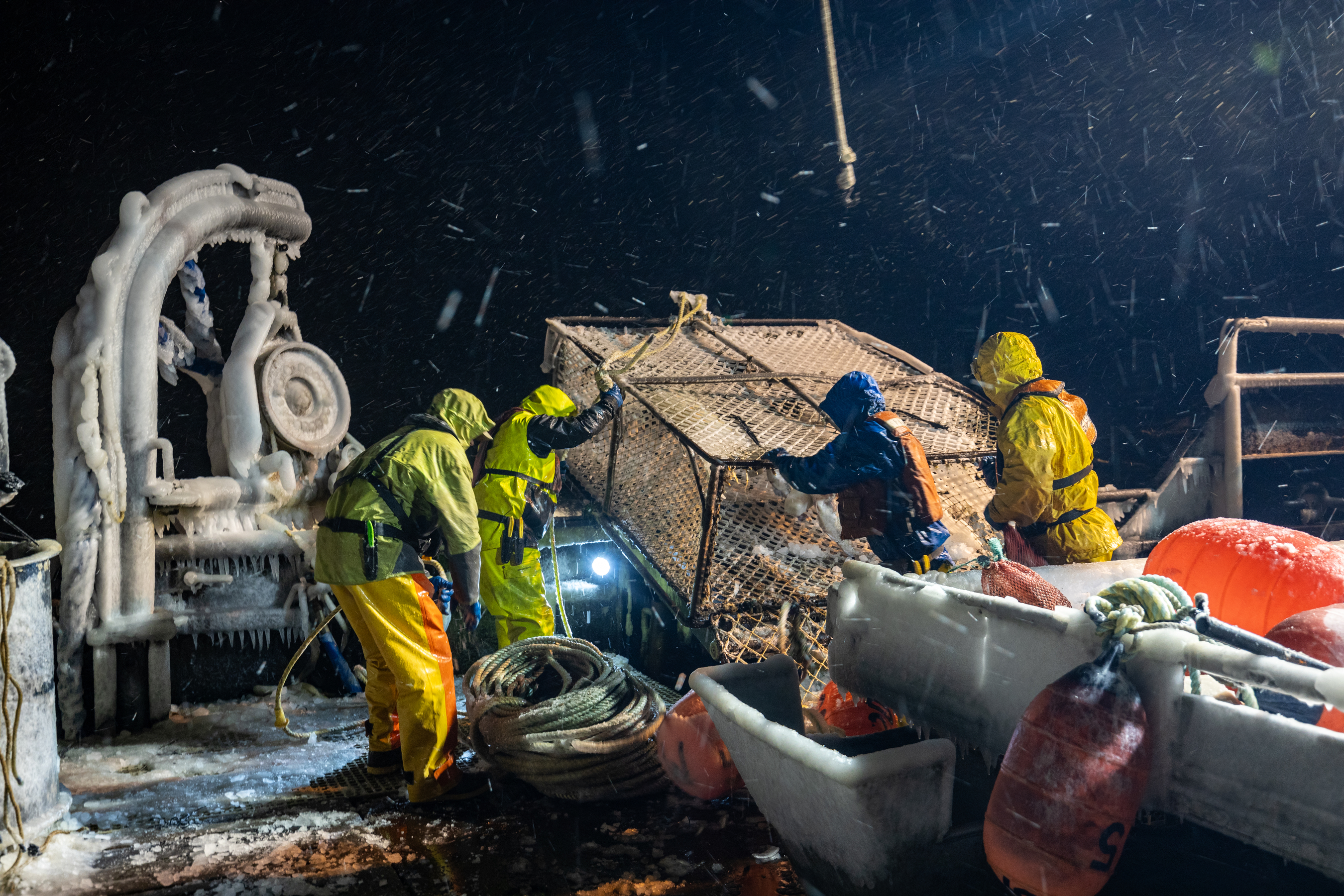 Four crew members in winter gear prepare an ice-cold fishing pot on a boat.