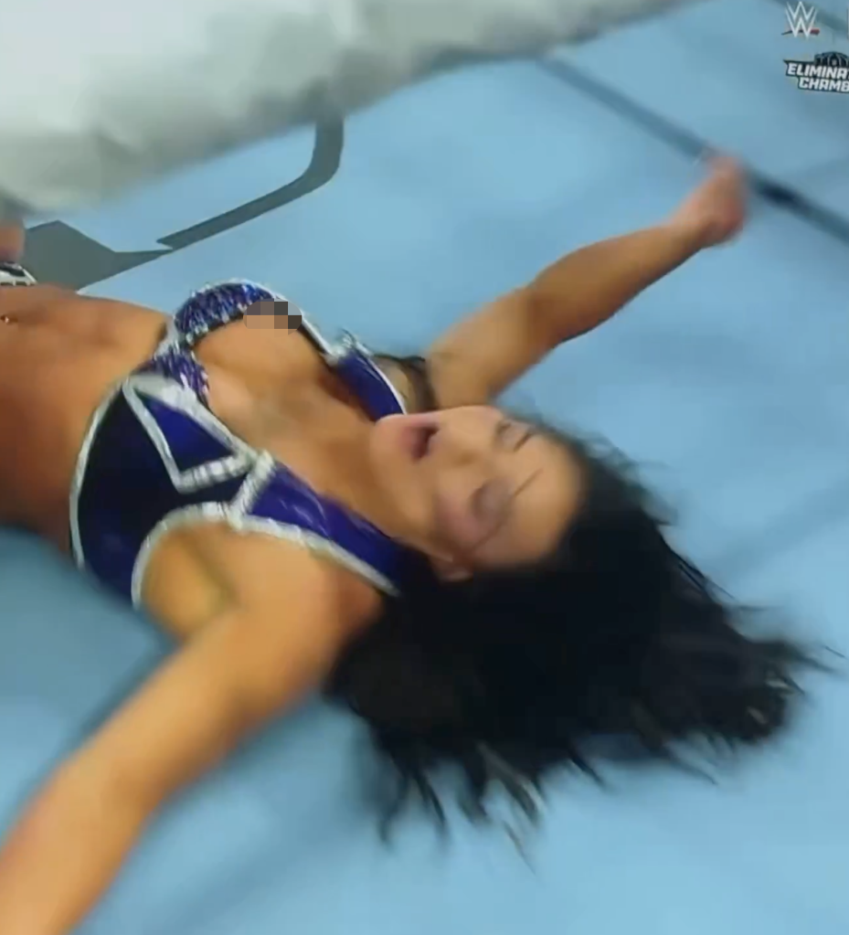 Kiana James, a WWE wrestler, lies on her back in the ring, arms outstretched, with a wardrobe malfunction.