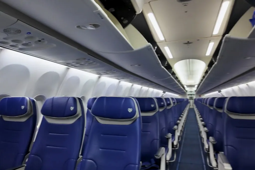 Interior of an empty Southwest Airlines plane with rows of blue seats and open overhead compartments.