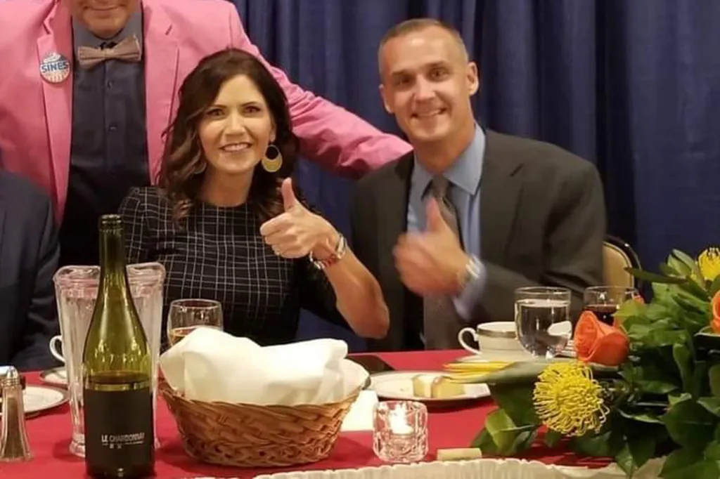 Kristi Noem and Corey Lewandowski giving thumbs up at a dinner table.