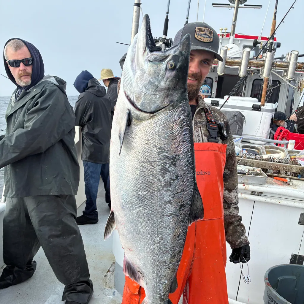 Man on a fishing boat holding up a large fish, while another man looks on.