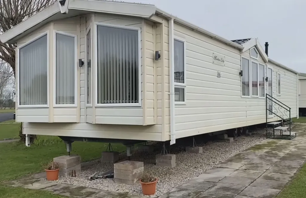 A 2013 Willerby Meridian caravan, cream-colored with white trim, is elevated on concrete blocks and gravel.
