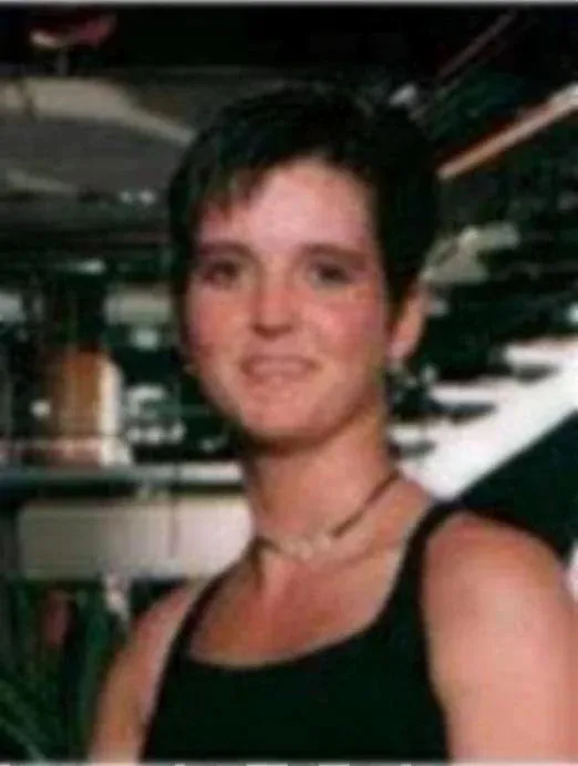 Amy Lynn Bradley, a white woman with short, dark hair and a light-colored choker necklace, smiling at the camera.