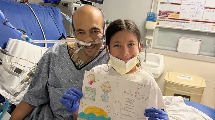 Rhett Pascual in a hospital bed with his daughter holding a 