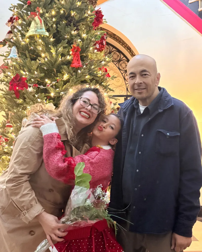 Rhett Pascual with his wife and daughter in front of a Christmas tree.