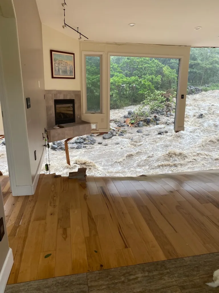 Floodwaters destroying a home, with a raging river flowing directly through the living room.