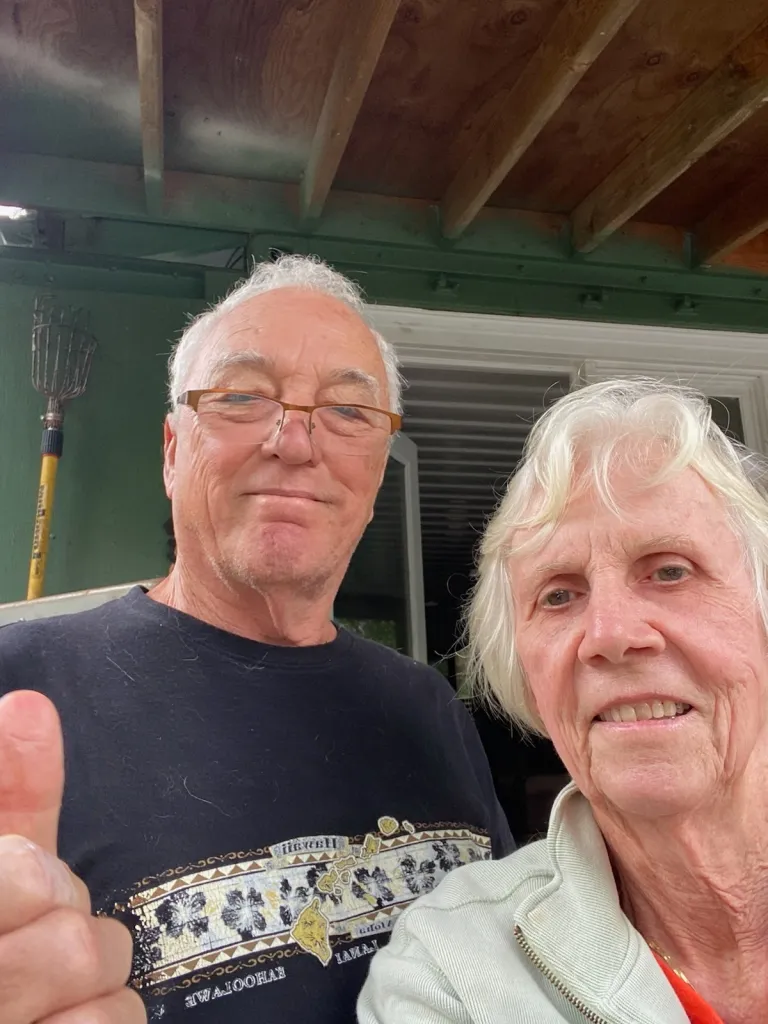 Carrie and Tom Bashaw, an older couple, stand together with Tom giving a thumbs up.