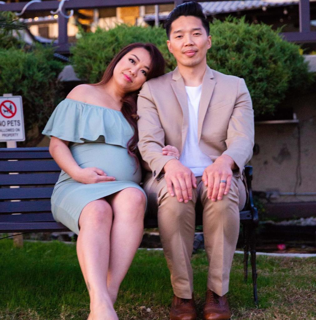 A pregnant woman in a light green dress leaning her head on the shoulder of a man in a tan suit, as they sit on a bench.