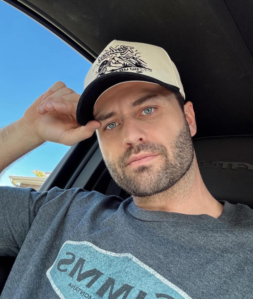 Dakota Mortensen in a car, wearing a gray t-shirt and a hat with a landscape design.