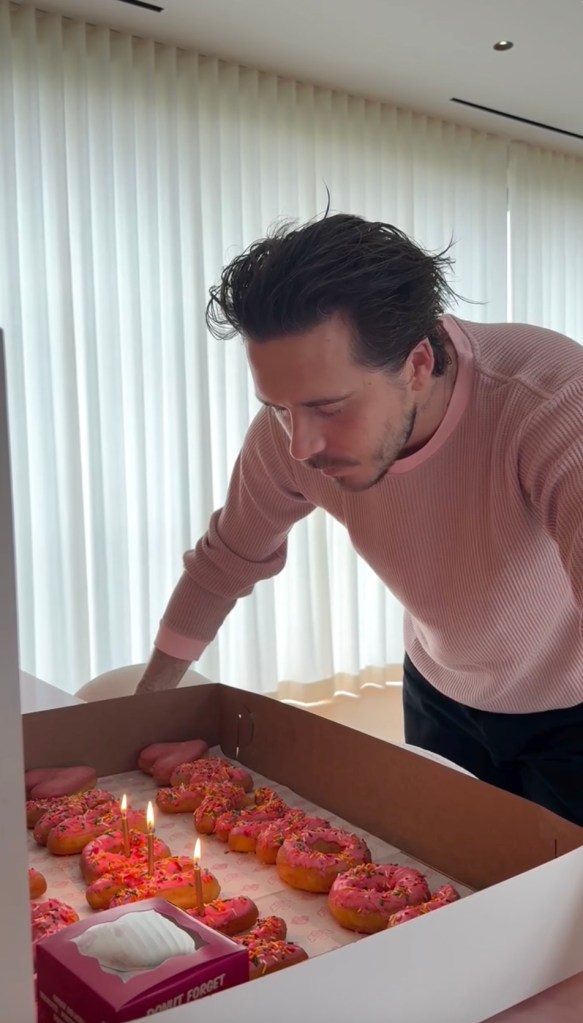 Brooklyn Beckham looking down at a box of birthday donuts with lit candles.