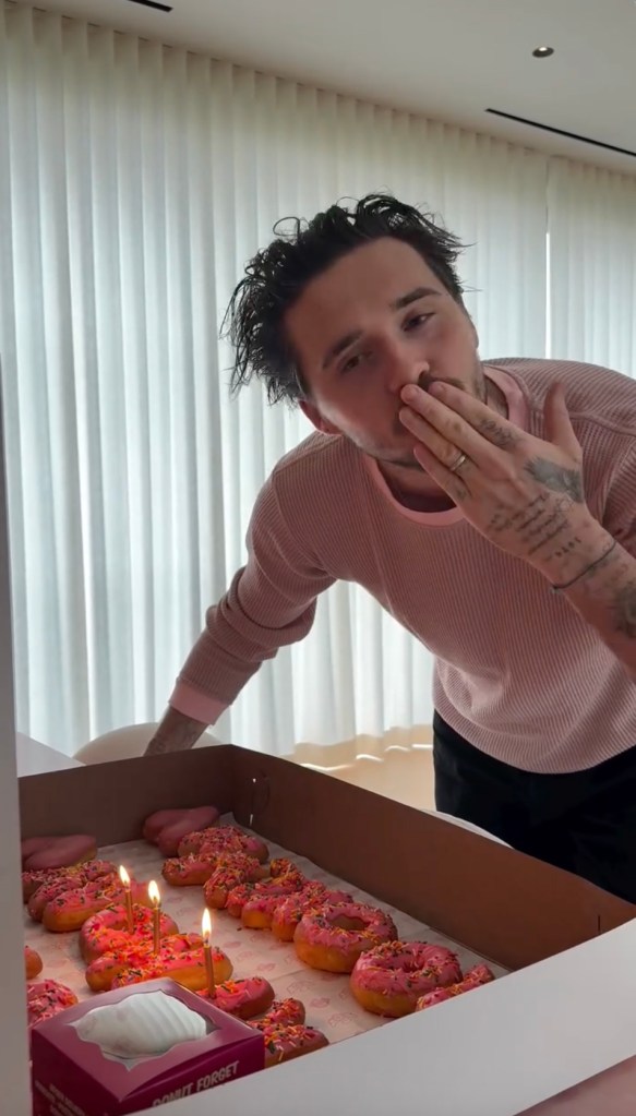 Brooklyn Beckham blowing a kiss over a box of donuts with candles.