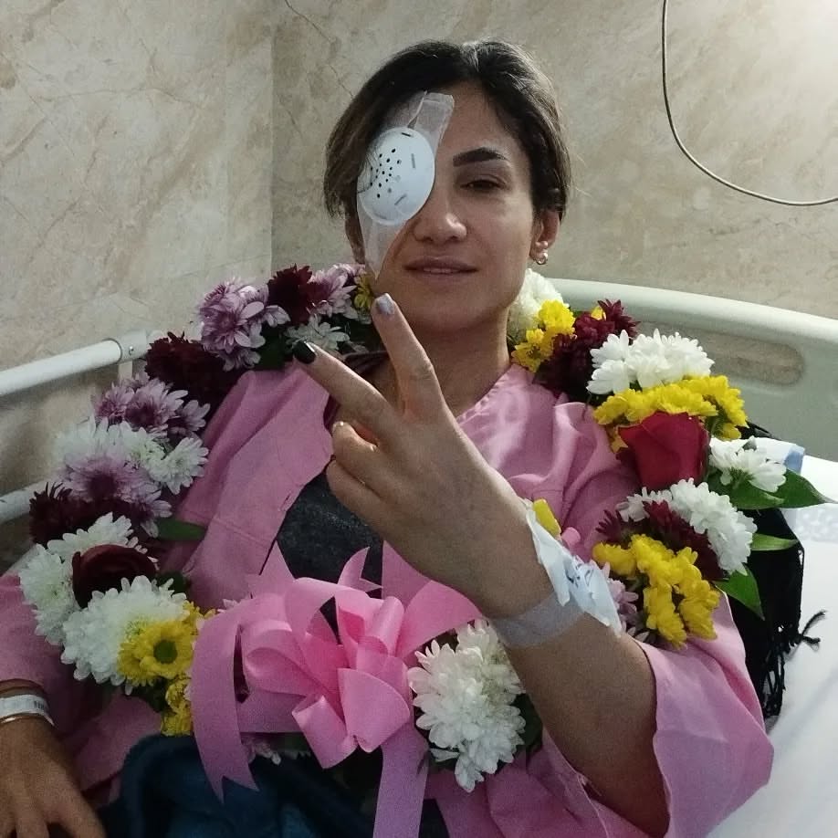 Mersedeh Shahinkar making a peace sign with flowers around her neck and an eye patch after being attacked with acid.
